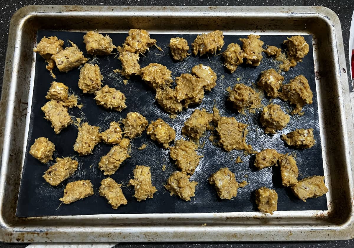 diced tempeh in thai peanut marinade spread out on a baking sheet covered in a baking mat.