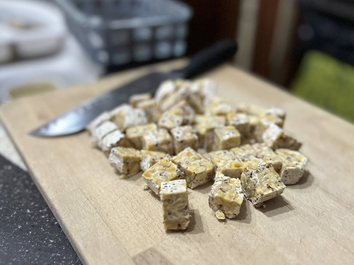 a wooden cutting board with diced chickpea tempeh and a knife on it.