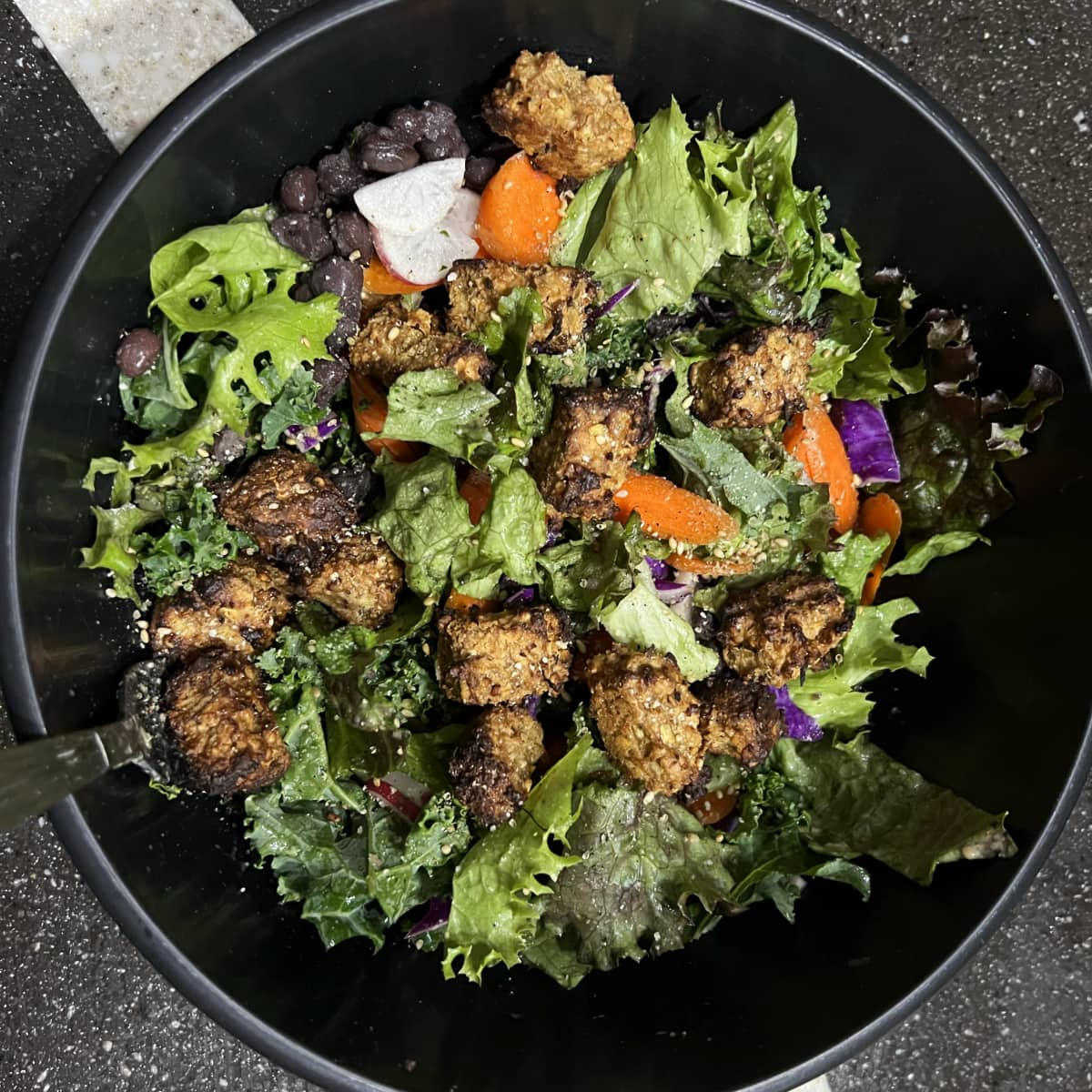 salad in a black bowl topped with thai peanut tempeh.