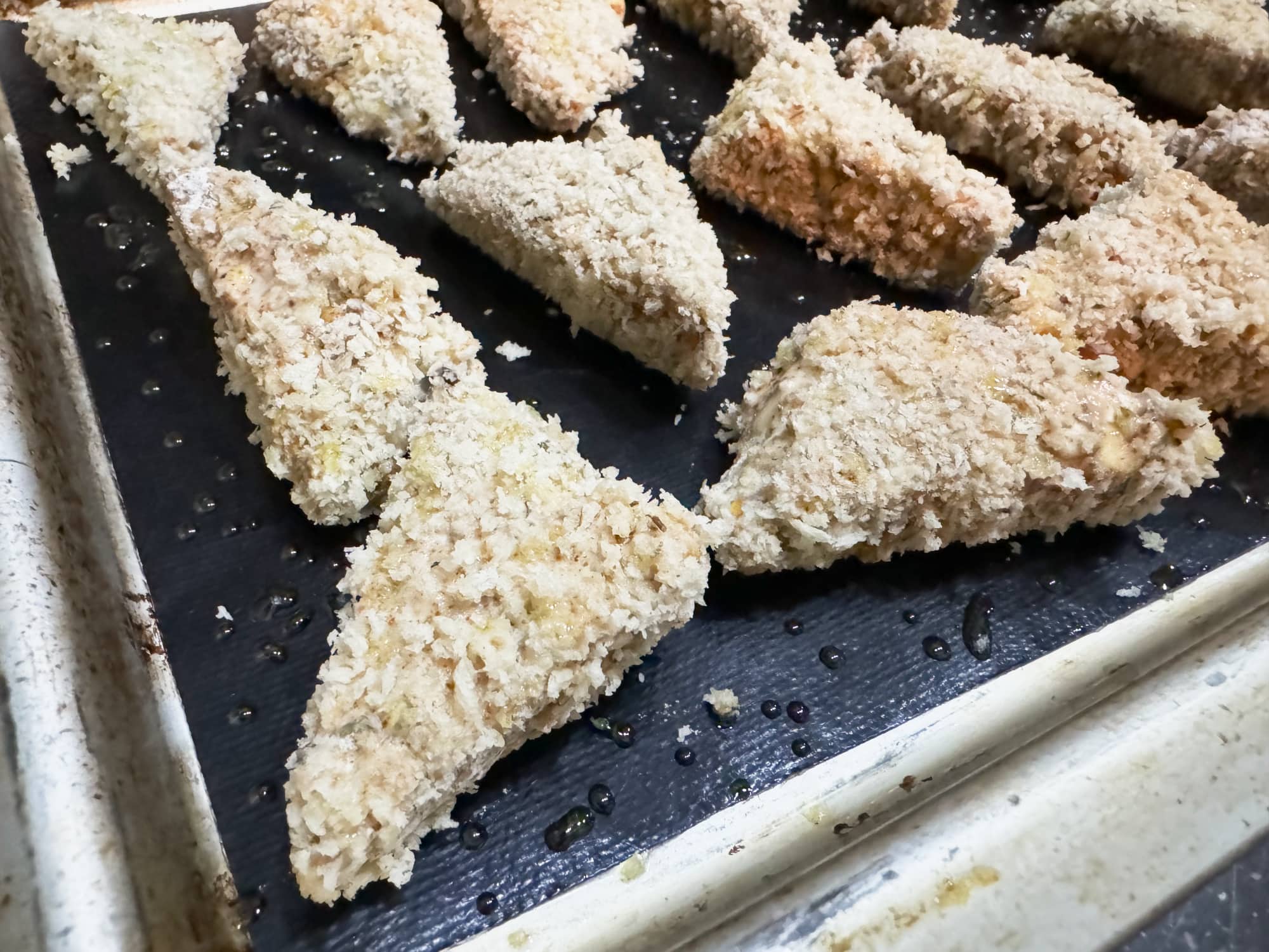 buffalo tempeh pieces coated in seasonings and panko and on a baking sheet ready to be baked.