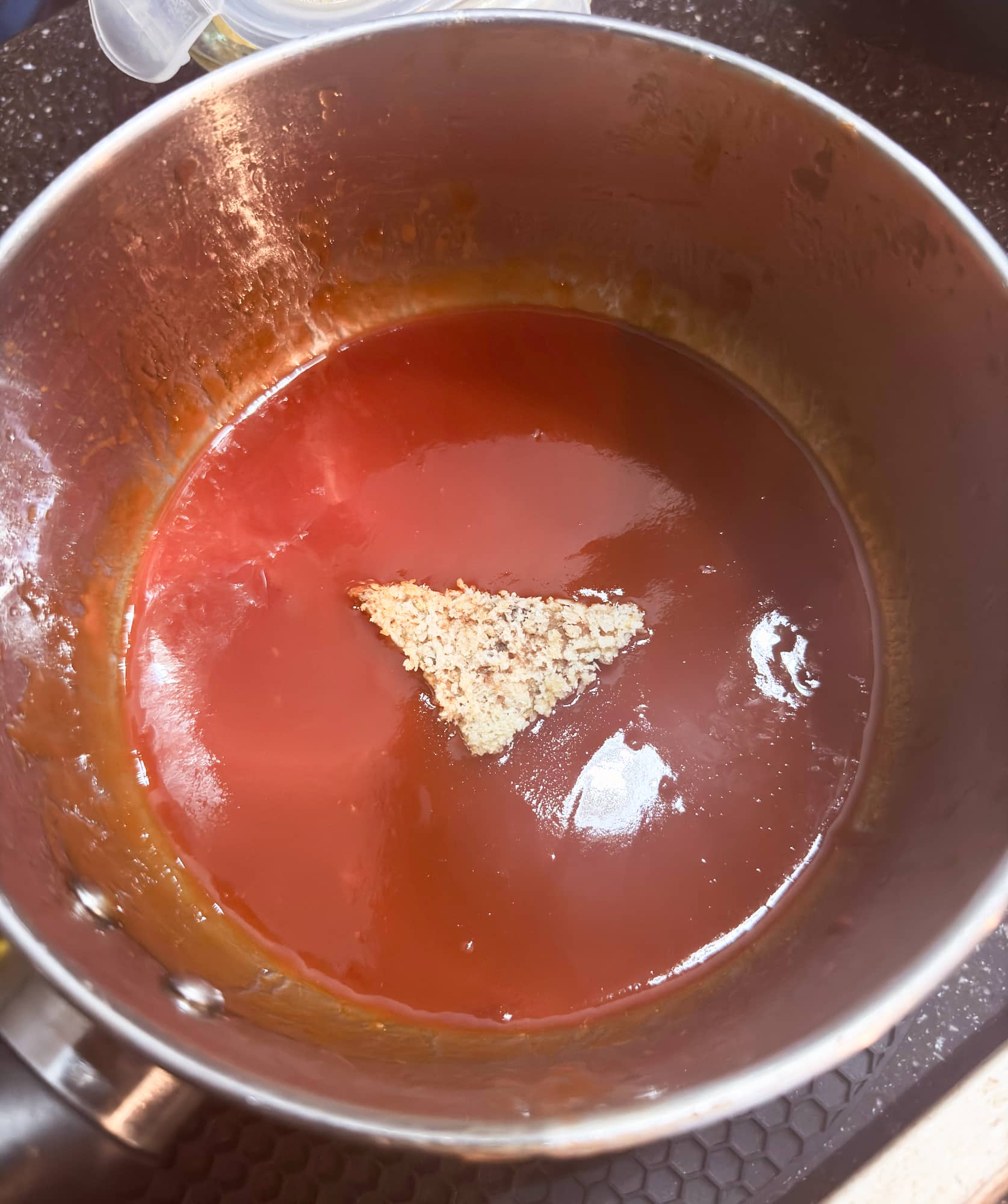 a piece of tempeh in a pot of vegan buffalo sauce.