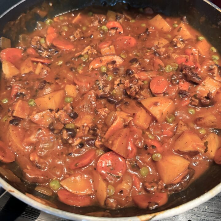 hearty tempeh stew close up in a pan on a stovetop.