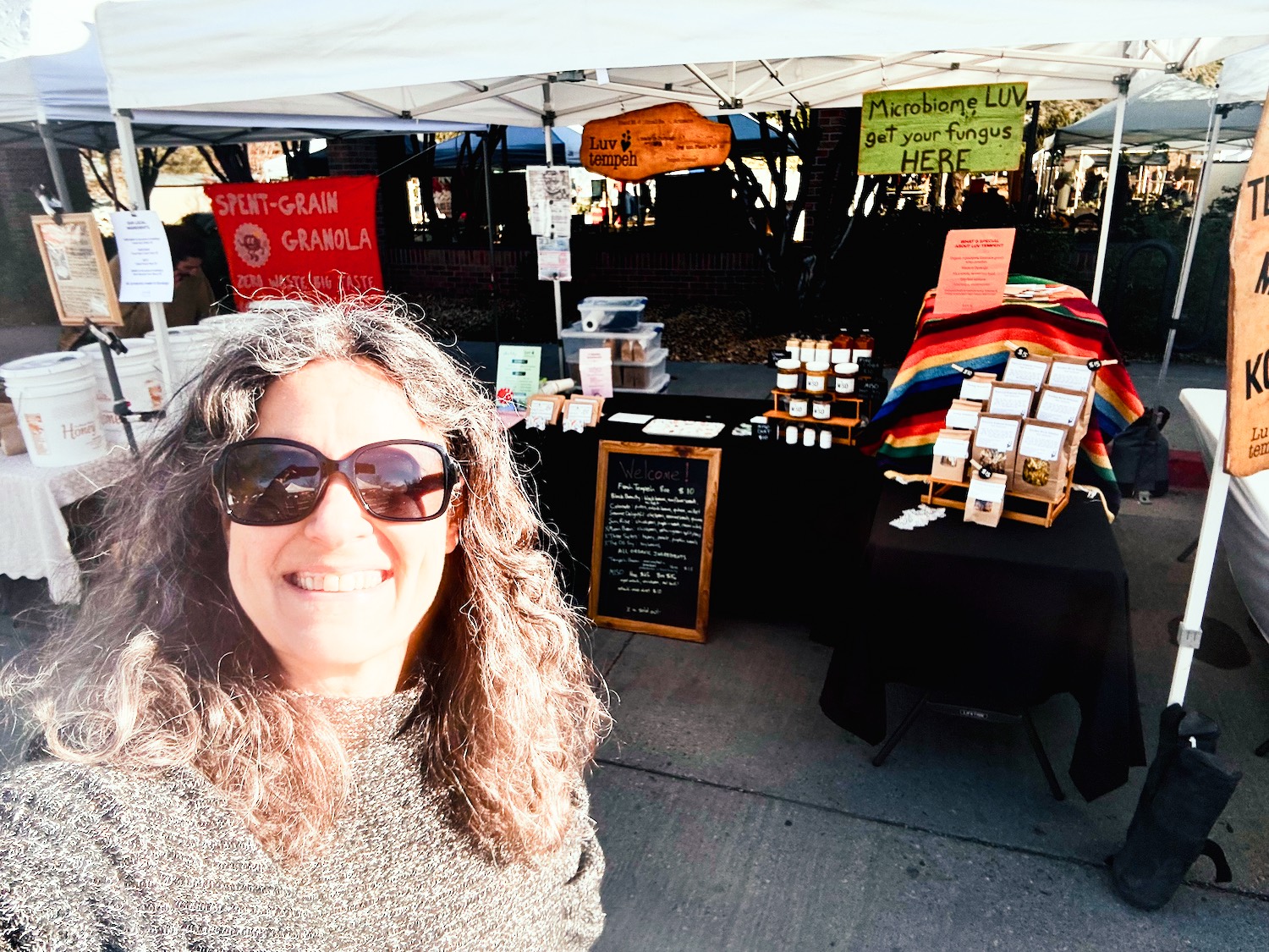 2025-dgo-farmers-market Laura in front of the Luv Tempeh booth at Durango Farmers Market in 2025.